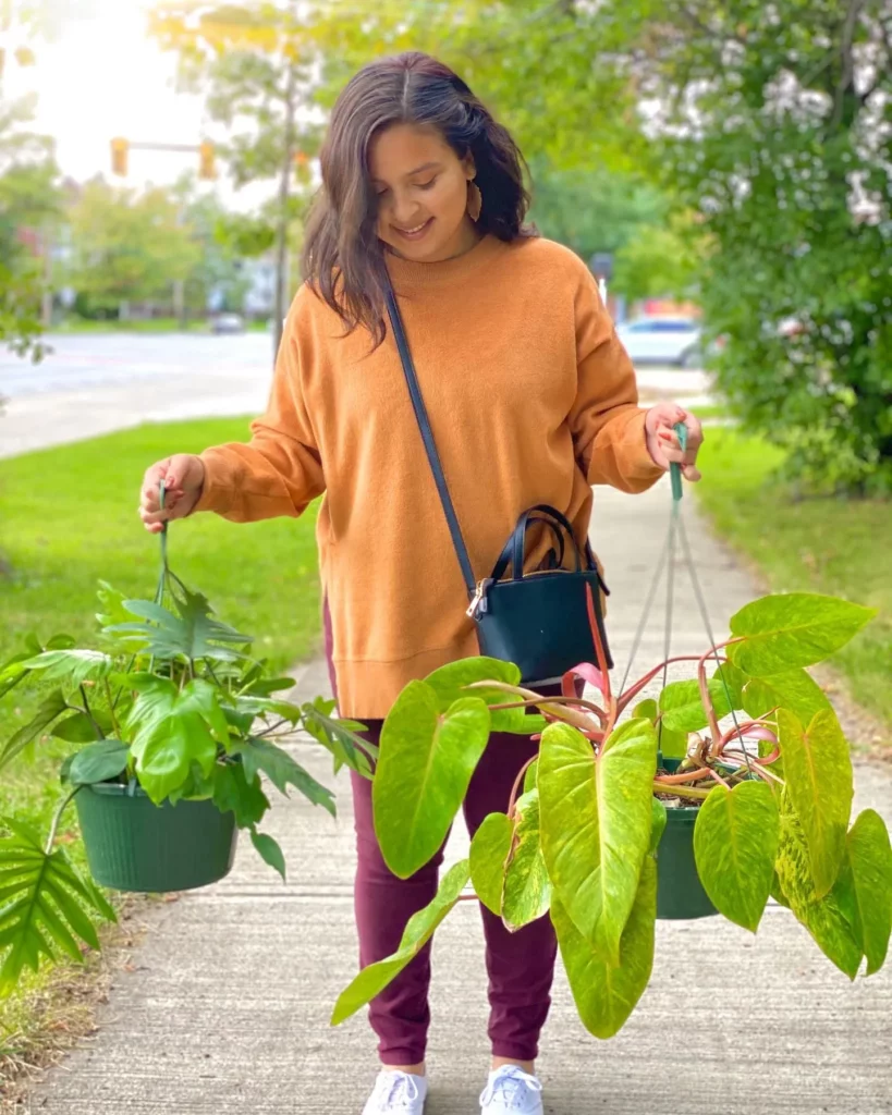 Teenage Girl Carrying Philodendron Tahiti Plant with Other Plants at Garden Pathway